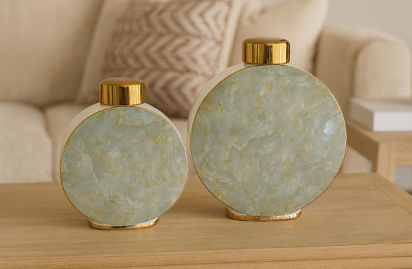 Two decorative vases with gold lids on a wooden surface, with a blurred background.