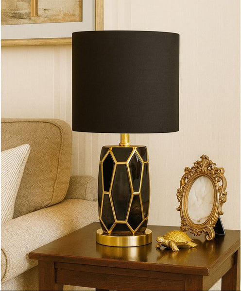 Decorative table lamp with black shade and gold base on a wooden table.