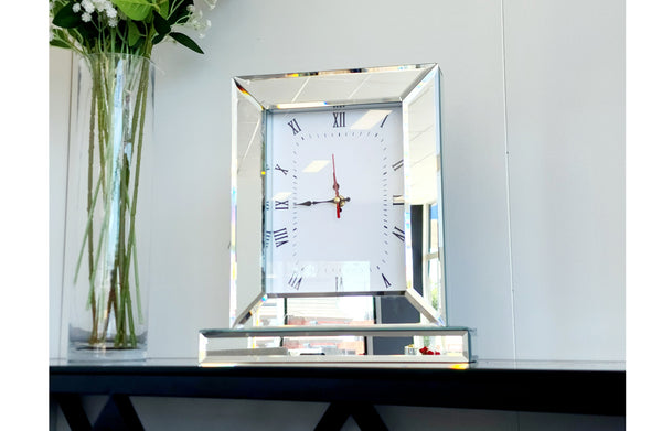 Silver mirrored Roman numeral clock styled beside flowers, adding elegance to home décor.