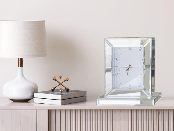Silver mirrored Roman numeral table clock styled beside lamp, enhancing room décor atmosphere.