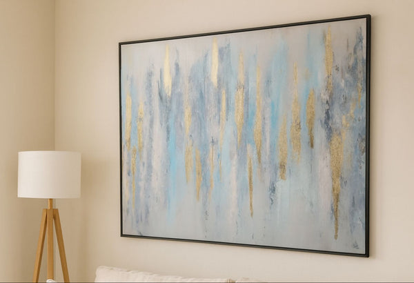 Abstract painting with blue and gold tones on a wall in a room with a lamp and bed.