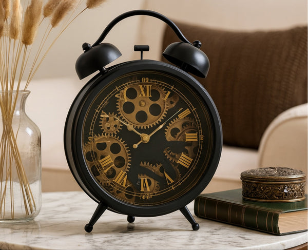 Decorative black and gold alarm clock on a table with books and a vase in the background