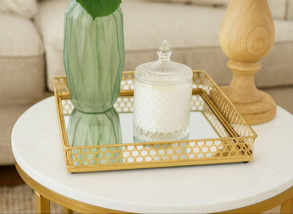 Gold mirror rectangle tray with a green vase and glass jar on a marble table