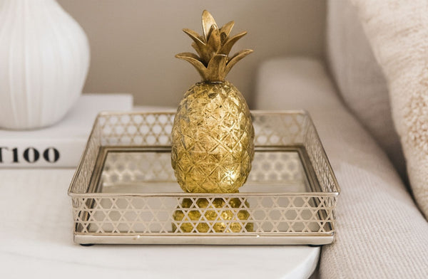 Decorative gold pineapple on a rectangle silver tray with a neutral background.