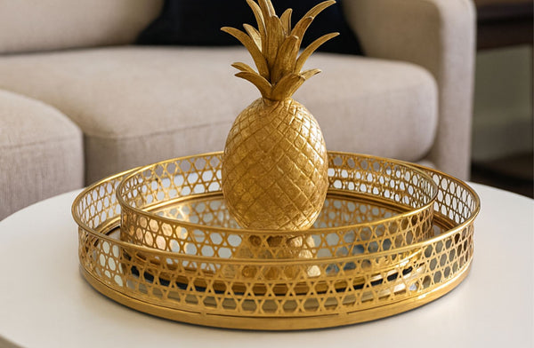 Gold pineapple decorative item on a matching gold round tray set on a table.