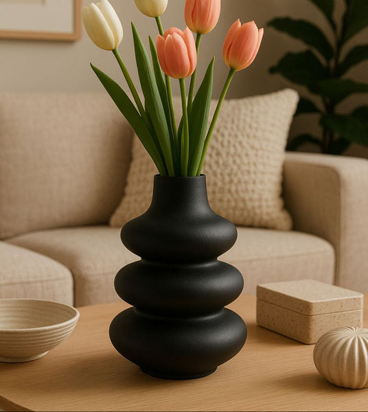 Black vase with pink and yellow tulips on a wooden table in a living room setting.