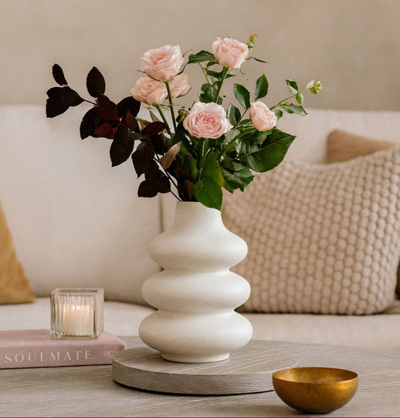 White vase with pink flowers on a table with a neutral background