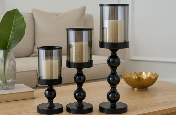 Set of black candle holders with candles on a wooden table in a living room setting.