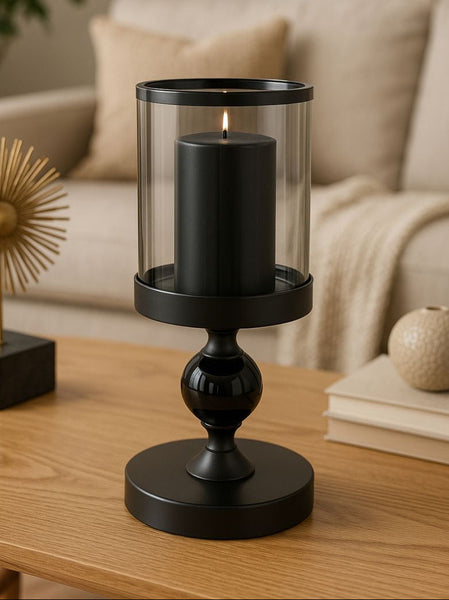 Black candle holder with a lit candle on a wooden table in a living room setting.