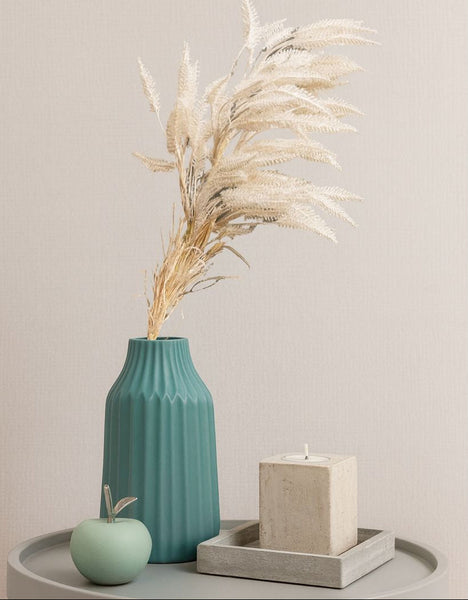Teal vase with pampas plants on a gray surface against a light gray background