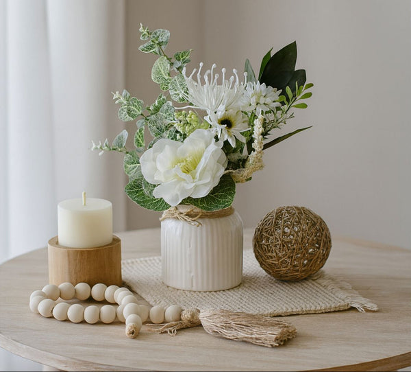 Decorative arrangement with flowers, candle, and beads on a table.