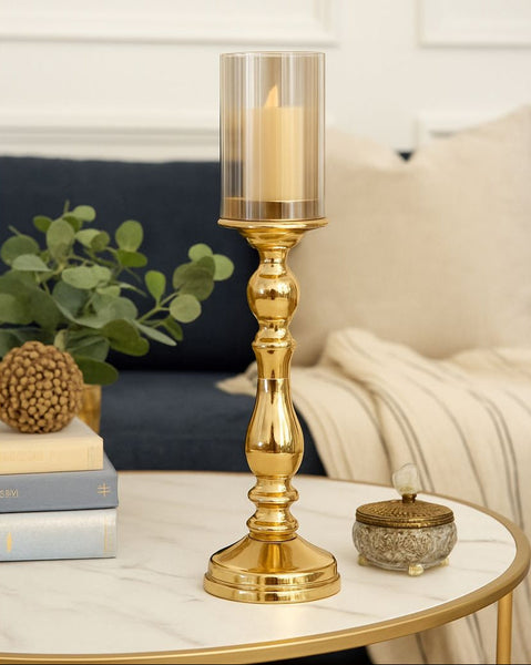 Gold candle holder with a lit candle on a table in a cozy living room setting.