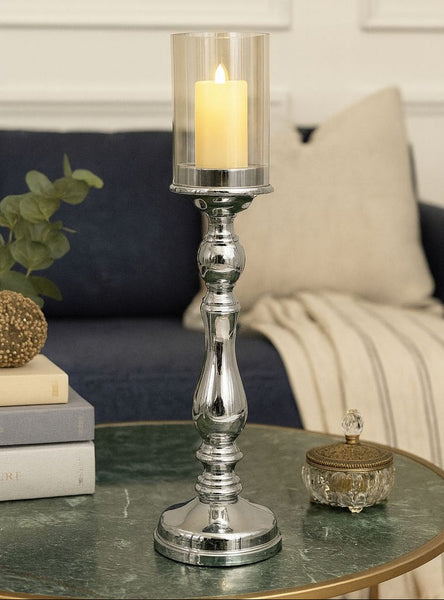 Silver candle holder with a lit candle on a table in a living room setting.