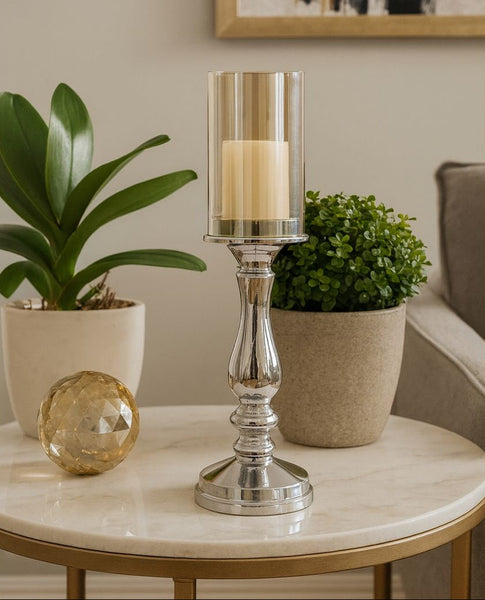 Silver candle holder with a candle on a marble table, surrounded by potted plants.