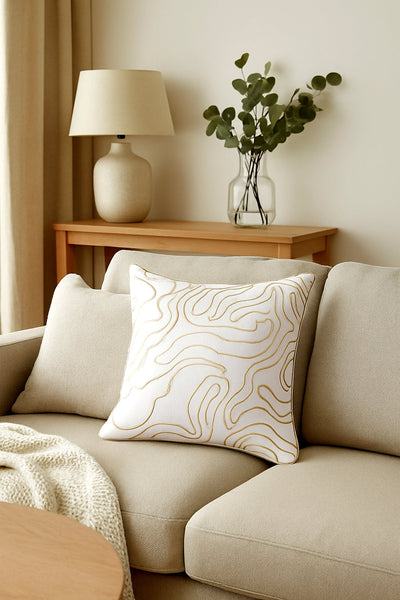 Cream and gold swirl cushion styled on beige sofa, adding elegance and luxury charm.