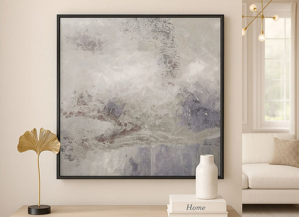 Abstract art piece with a hint of silver with black border on a wall in a living room setting with decor elements.
