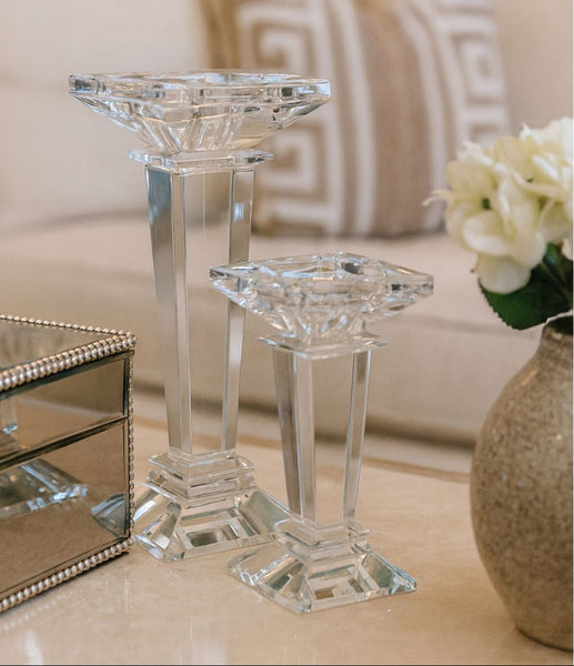 Crystal candle holders on a table with a vase of flowers in the background