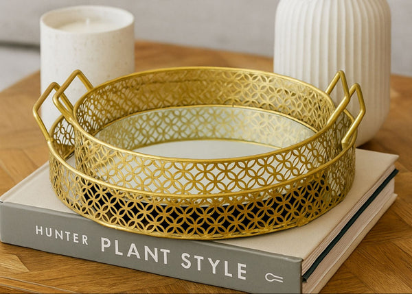 Gold decorative tray set on a book with a candle and vase in the background