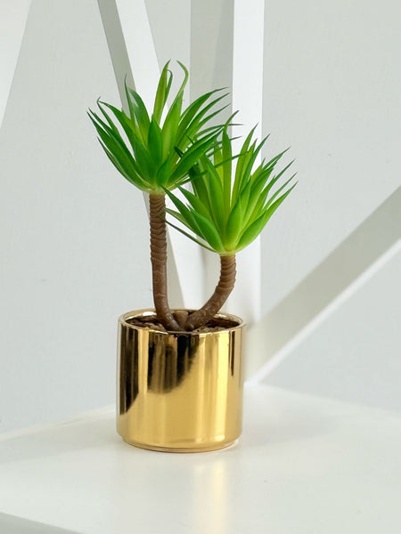 Faux green succulent in a shiny gold metal pot, displayed on a modern white shelf.