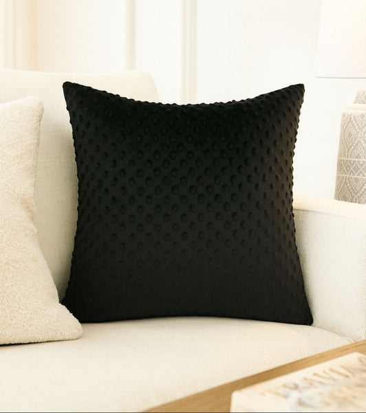 Black textured pillow on a beige sofa with a white wall background
