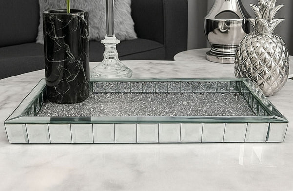 Decorative mirrored tray on a marble surface with decorative items in the background