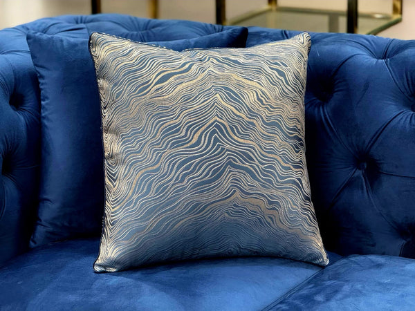 Atlantis Blue Designer Cushion styled on blue sofa, luxury accent pillow with gold wave pattern