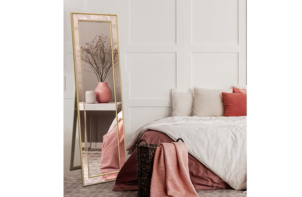 Free standing gold beaded framed mirror styled beside bed with soft décor.