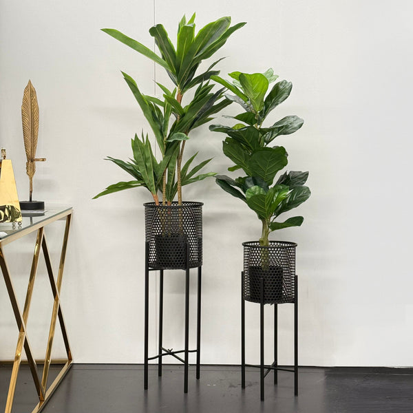 Black beehive planters on foldable black stands, styled indoors with tall green plants. Displayed against a plain white wall and dark flooring.