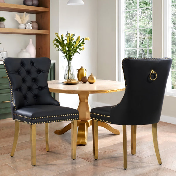 Pair of black PU leather tufted dining chairs with gold stainless steel legs styled around a round wooden dining table in a modern dining room.