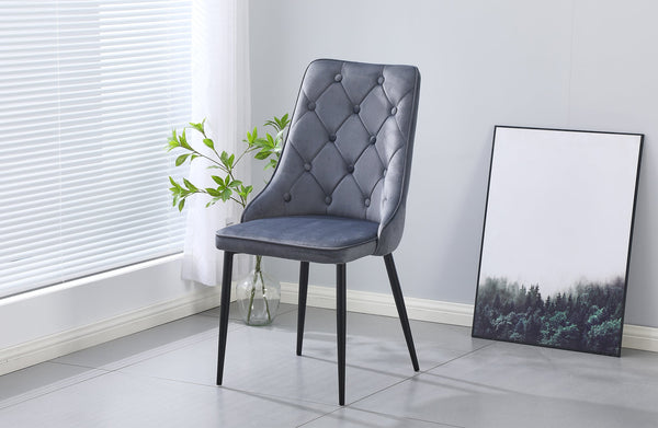 Grey velvet button tufted dining chair with black legs styled in a modern dining room.