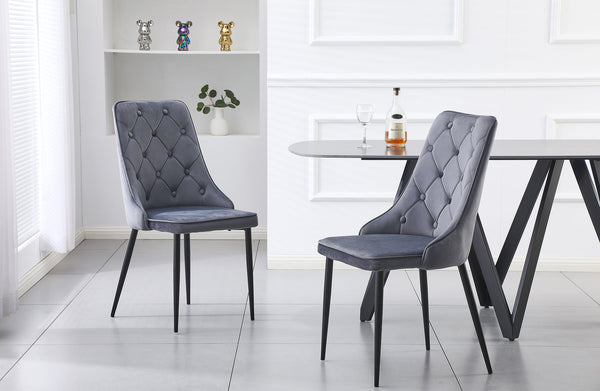 Pair of grey velvet button tufted dining chairs with black legs styled with dining table.