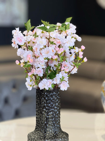 Elegant light pink artificial cherry blossoms beautifully arranged in a textured black vase.
