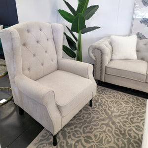 Beige Chesterfield tufted armchair displayed in showroom with matching sofa and rug