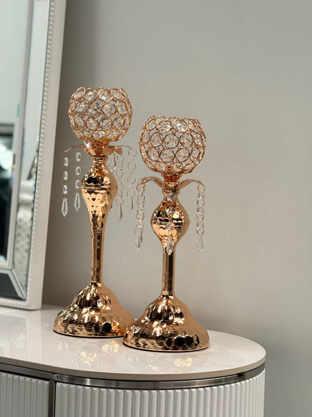 Stylish gold crystal ball candle holders displayed on a tabletop with lush green background — featuring shimmering crystals and a hammered gold base for an elegant decorative touch.