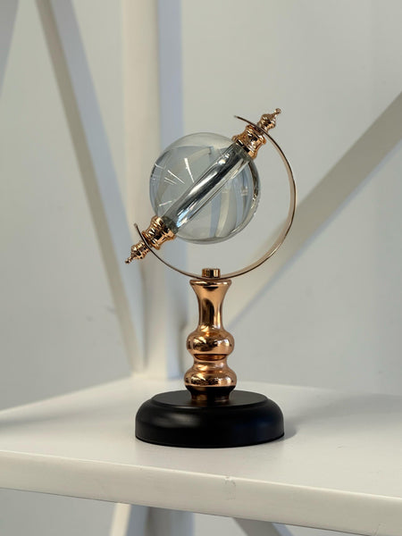 Crystal globe in gold with black base styled on white shelf.