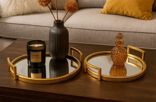 Decorative setup with two mirrored gold trays, a candle, and a vase on a wooden surface.