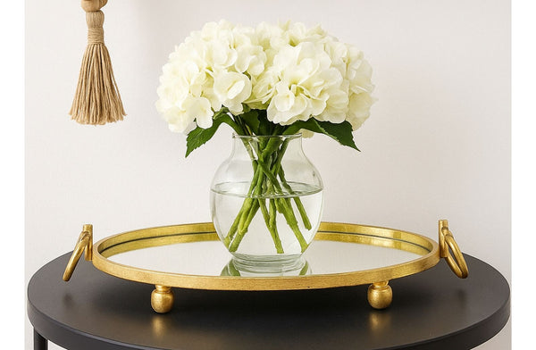 Gold mirrored tray with a vase of white flowers on a black surface
