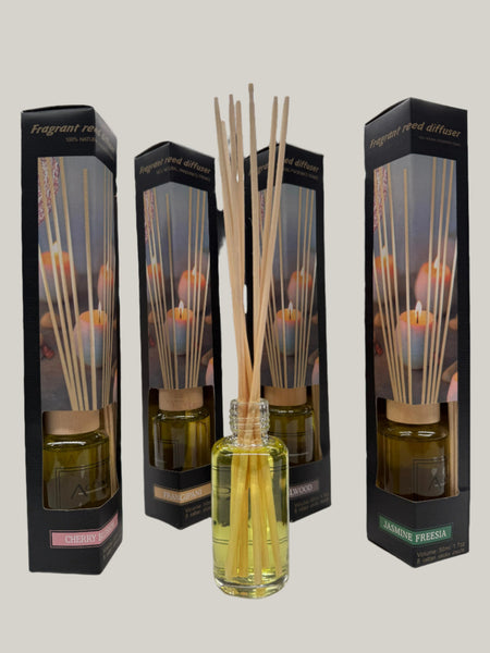 Fragrant reed diffuser with natural reeds displayed in an open glass bottle, surrounded by boxed scents including Cherry Blossom, Sandalwood, and Jasmine Freesia