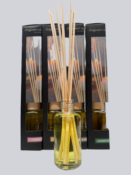 Front-facing view of a fragrant reed diffuser with reeds in a glass bottle, placed in front of boxed scents including Cherry Blossom, Sandalwood, and Jasmine Freesia