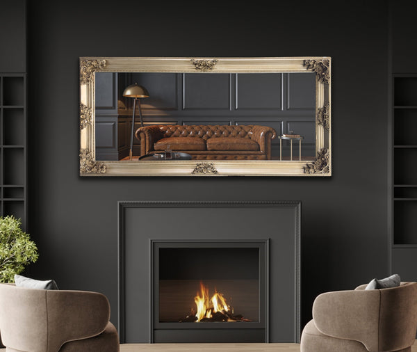 Champagne French provincial ornate deluxe mirror styled horizontally above fireplace with armchairs and décor.