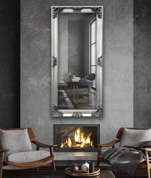 Silver French provincial deluxe mirror styled vertically above fireplace with grey chairs and décor.