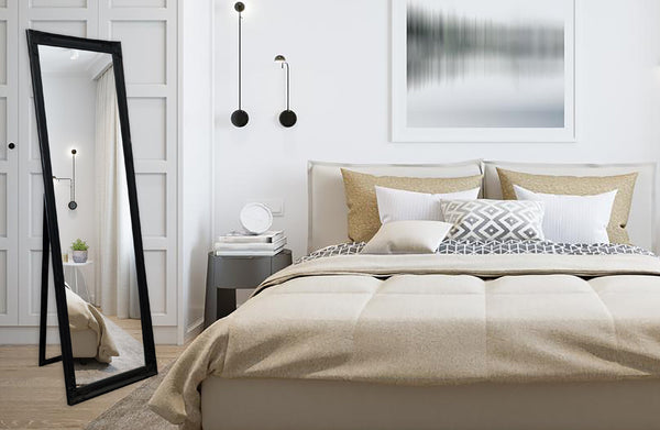 Black French provincial free standing mirror styled in bedroom with beige bedding and wall art.