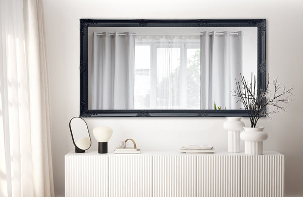 Black French provincial ornate mirror styled horizontally above console with vases and décor accents.