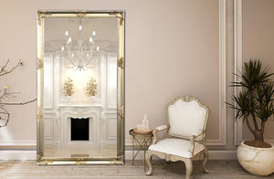 Champagne ornate French provincial mirror styled with armchair and fireplace in elegant interior décor.