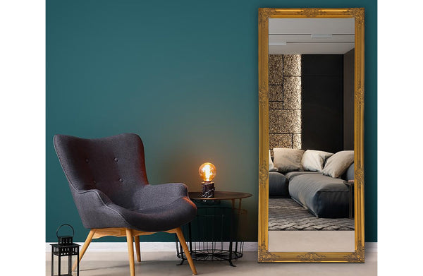 Gold French provincial ornate mirror styled beside teal wall, armchair and cozy bedroom corner.