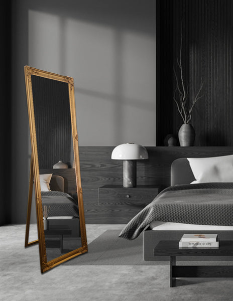 Gold French provincial free standing mirror styled in dark bedroom with grey bed and lamp.