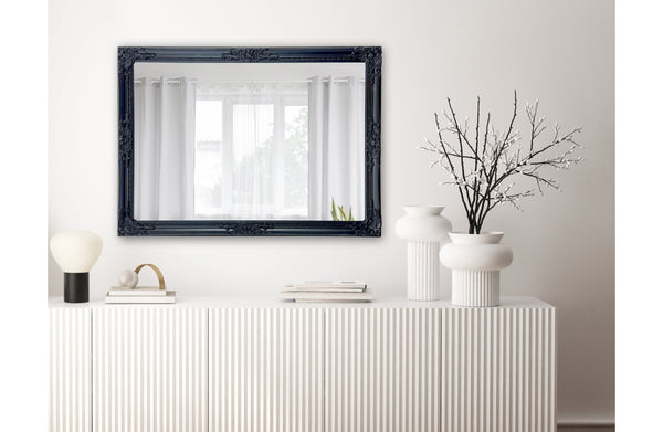 Silver French provincial ornate mirror styled on dark wall with chandelier and modern armchair.