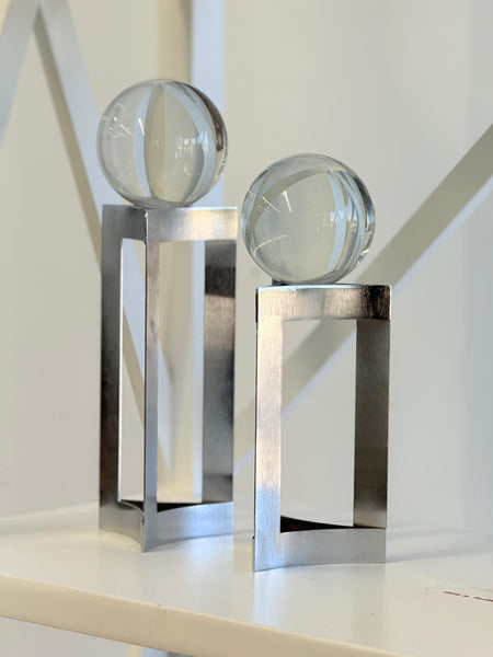Silver glass sphere décor pair styled on shelf with soft lighting.