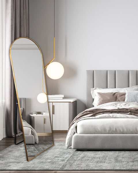 Elegant gold free-standing arch mirror in modern bedroom beside grey bed and pendant light.