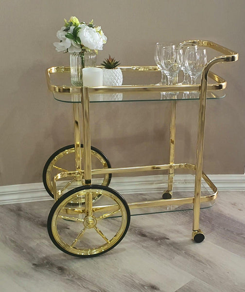 Elegant gold drink trolley with glass top, flowers, and glassware setup.